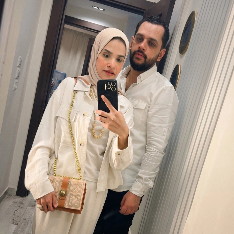 A mirror selfie of Dr. Noor Abdelbasst in an elegant white outfit standing next to her husband Mostafa in a white shirt.