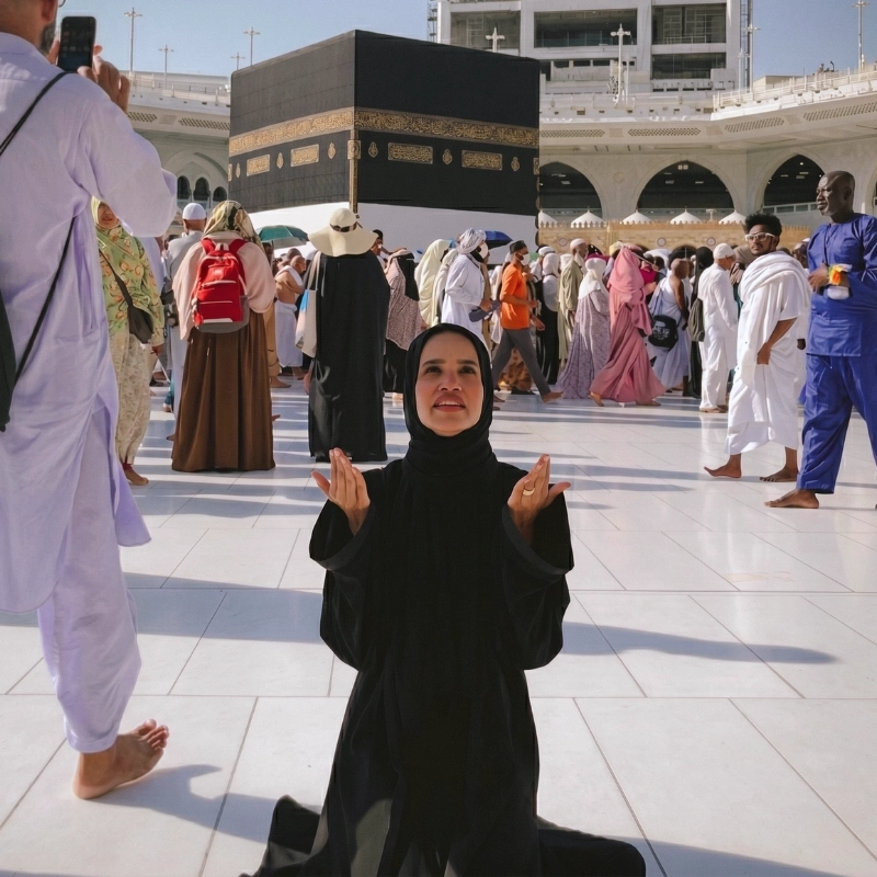 Dr. Noor Abdelbasst wearing a black abaya, kneeling and praying with open palms in front of the Holy Kaaba in Mecca during Hajj.